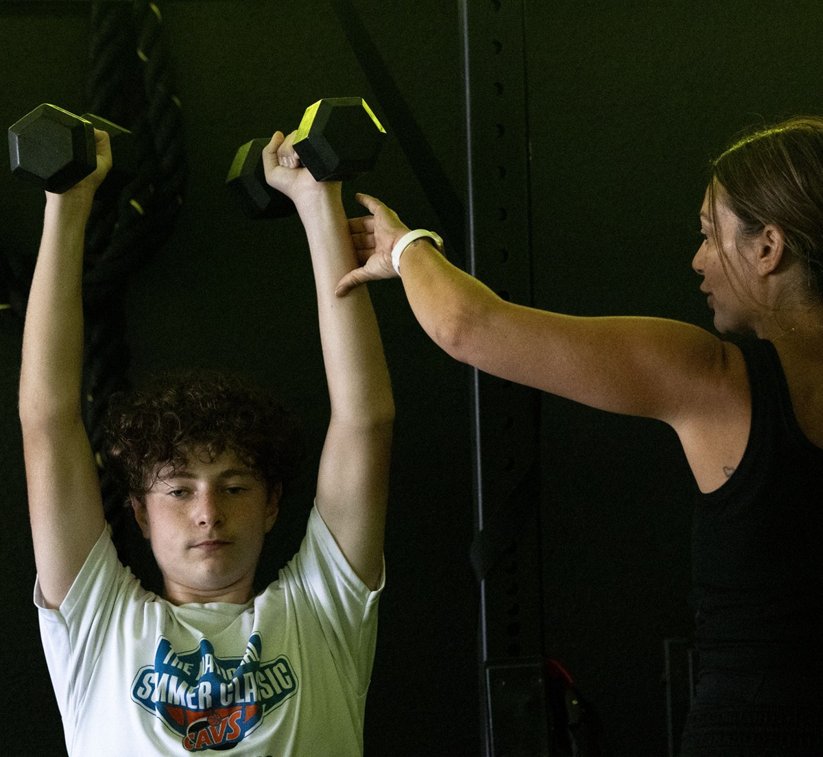 Teen lifting weights while coach corrects form at XFIT